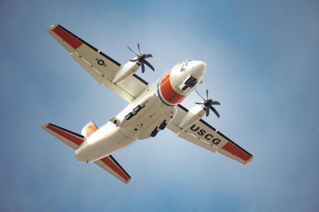 A USCG aircraft flies high against a clear blue sky, showcasing its distinct markings.